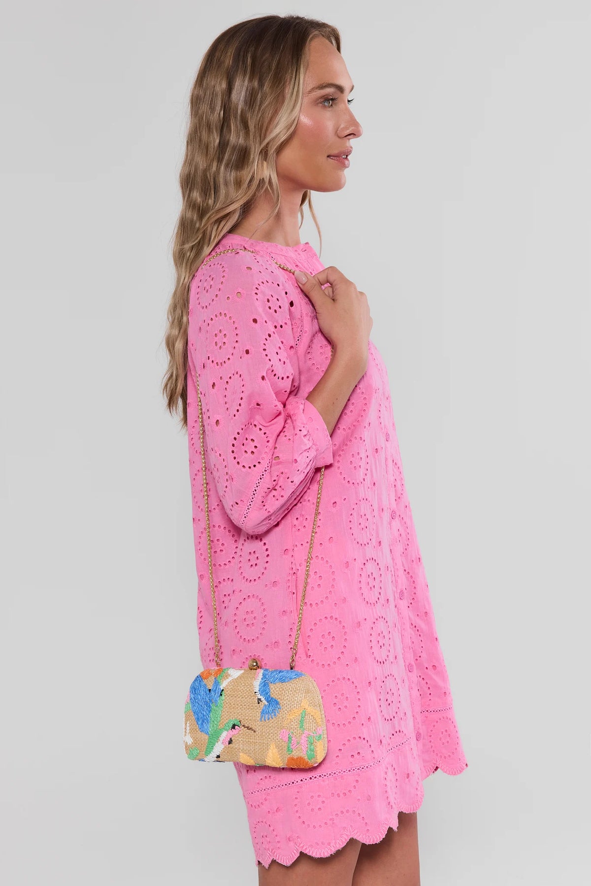 Woman wearing a pink lace dress holding a colorful handbag on a plain background