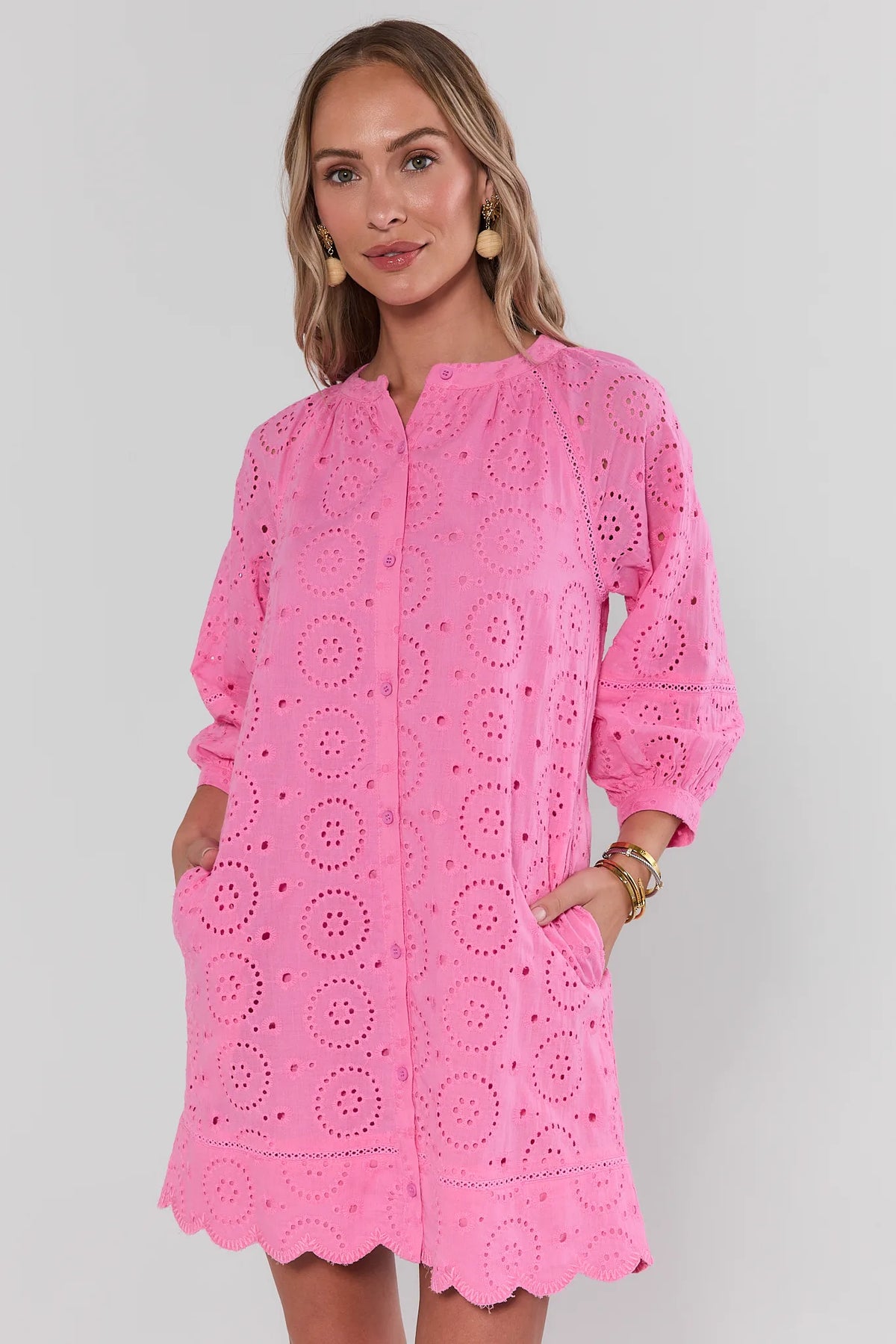 Pink eyelet short dress angled view showing side pockets and button-front detail | Avara