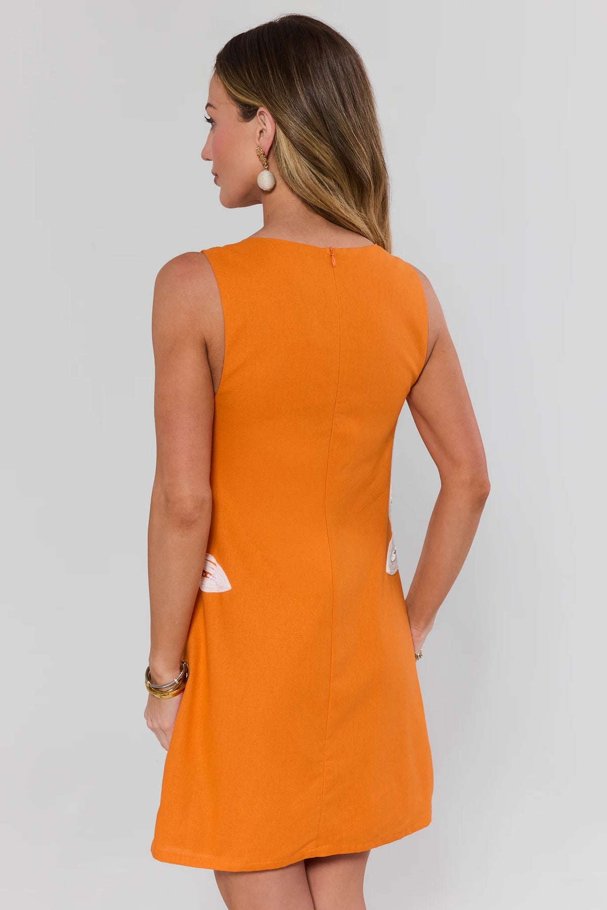 Orange embroidered short dress back view showing center seam, zip closure, and side white floral detail | Avara
