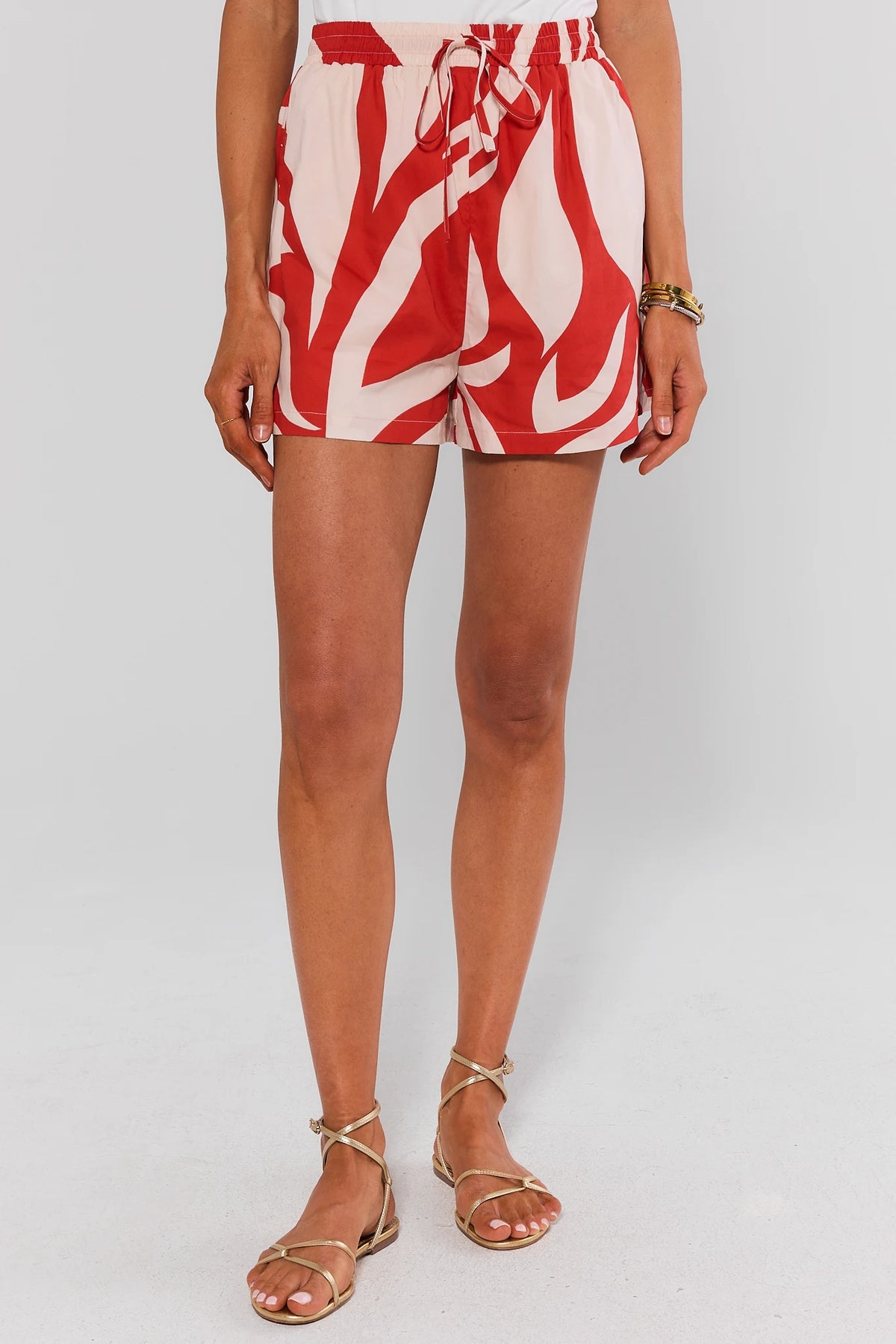 Red printed drawstring shorts styled with white tank and gold sandals, full front view on model | Avara