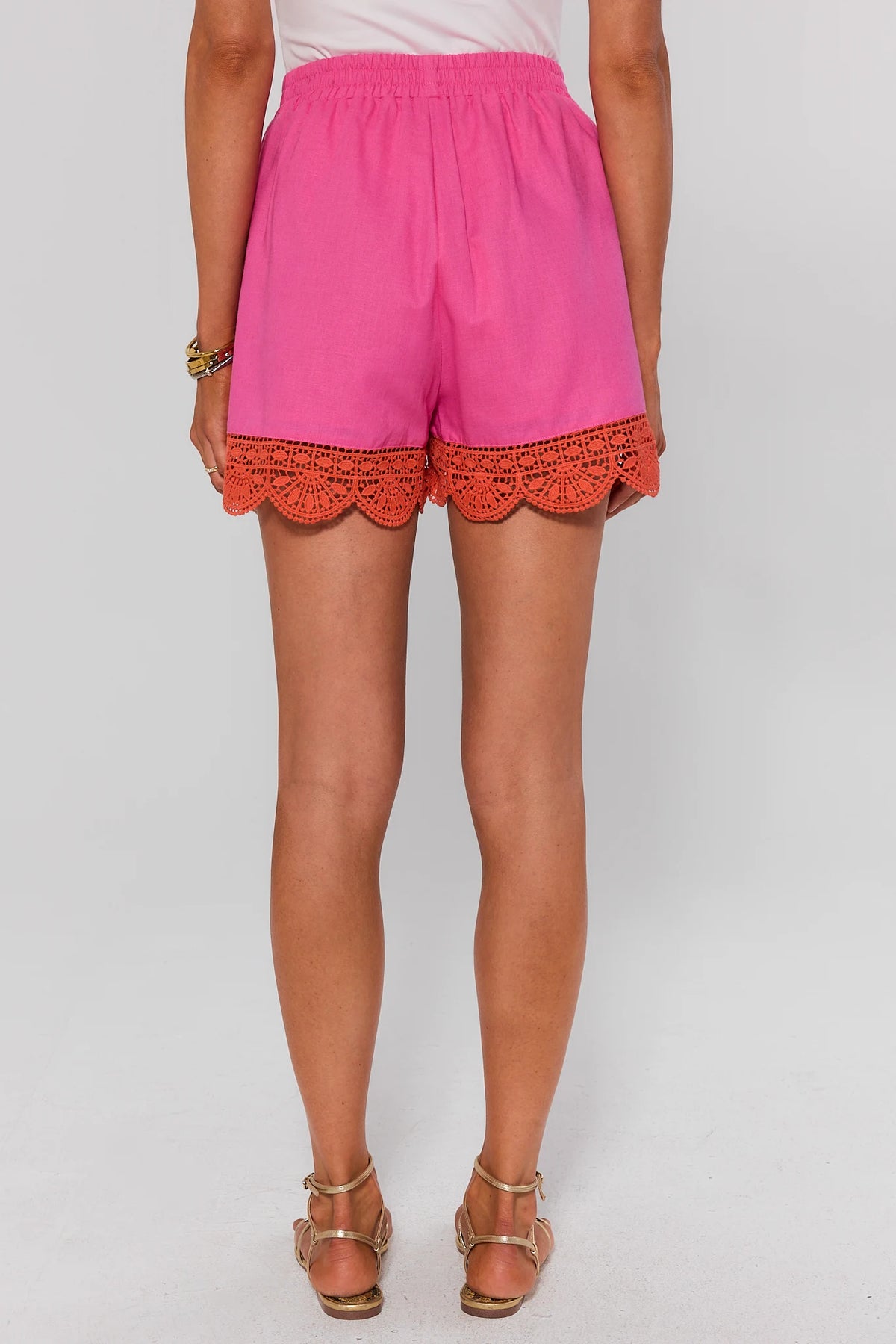 Pink shorts with coral eyelet crochet trim, back view showing scalloped hem and elastic waistband | Avara