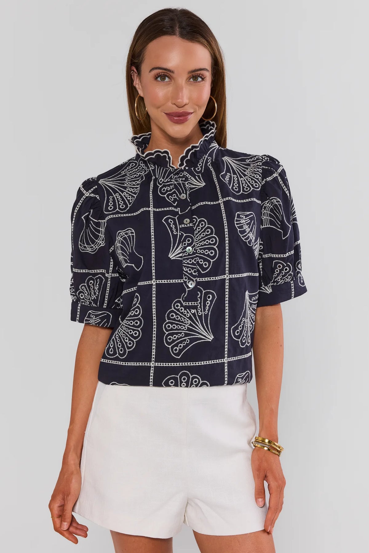 Navy seashell embroidered top with ruffle neckline and puff sleeves, styled with white shorts - Front View | Avara