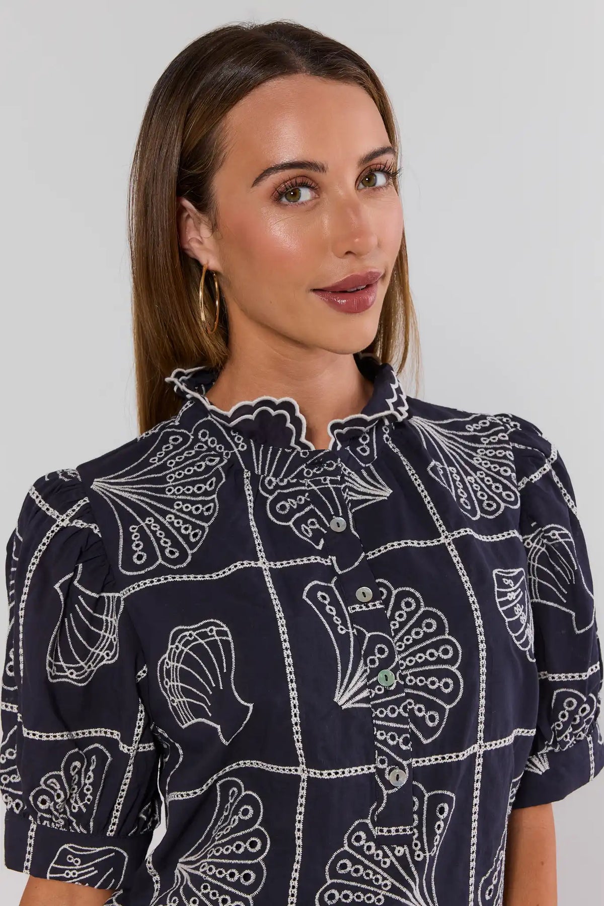 Navy blue seashell embroidered top close-up showing scallop ruffle neckline and white embroidery detail | Avara