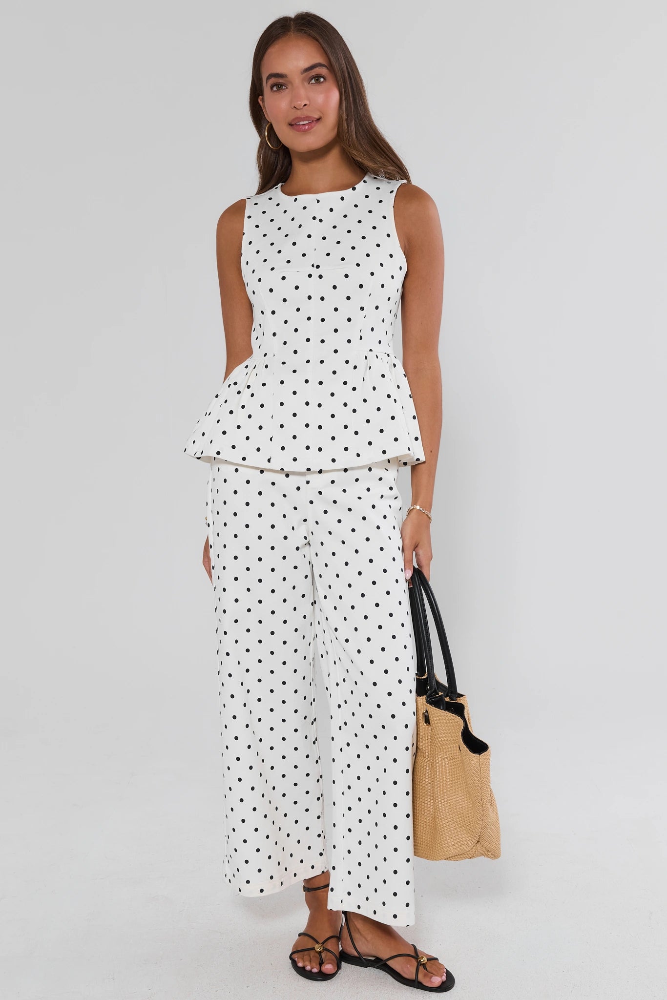 White polka dot wide leg pants styled with matching peplum top and rattan bag - Full Length On Model | Avara