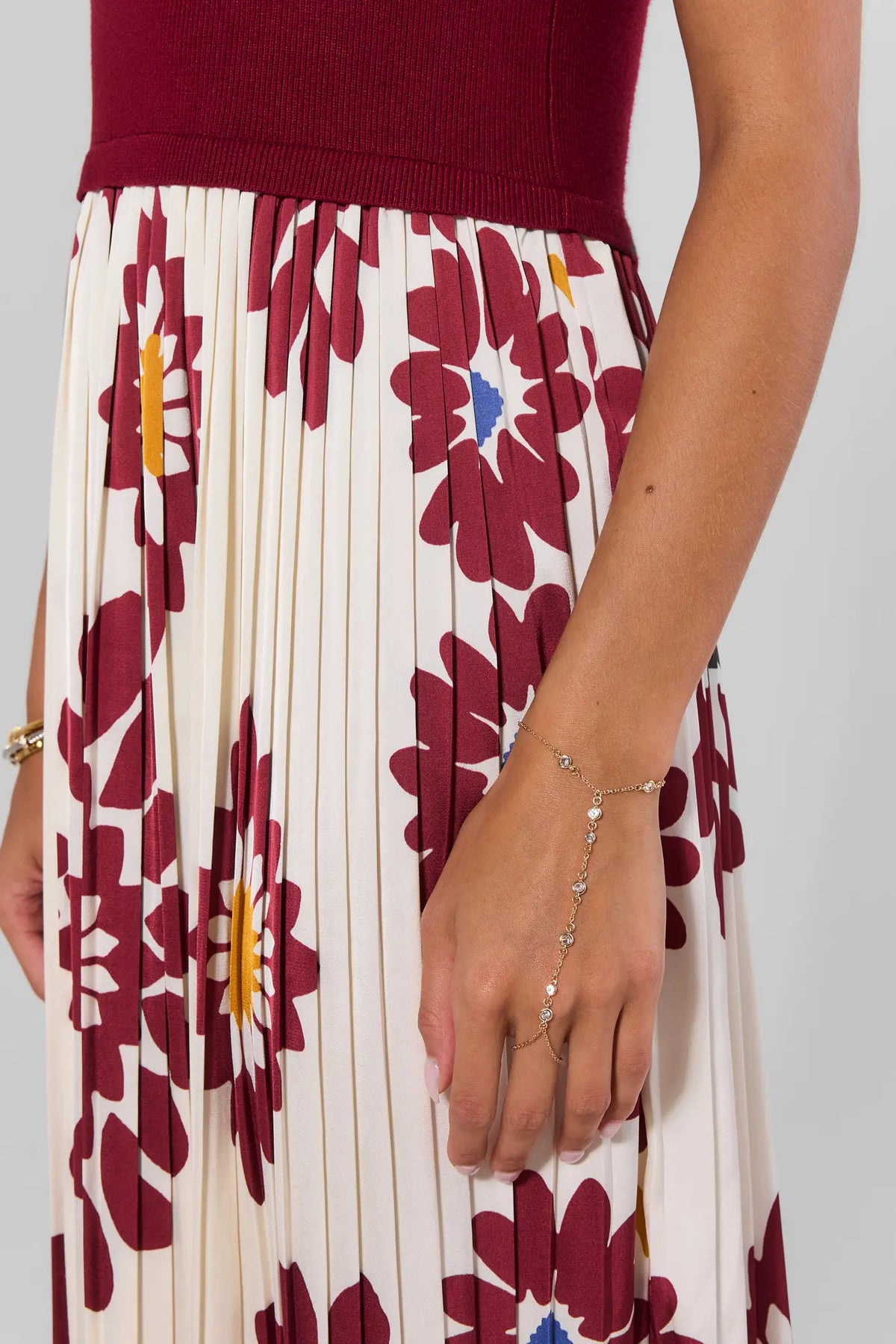 Woman wearing gold hand chain bracelet with rhinestone details styled with floral skirt | Avara