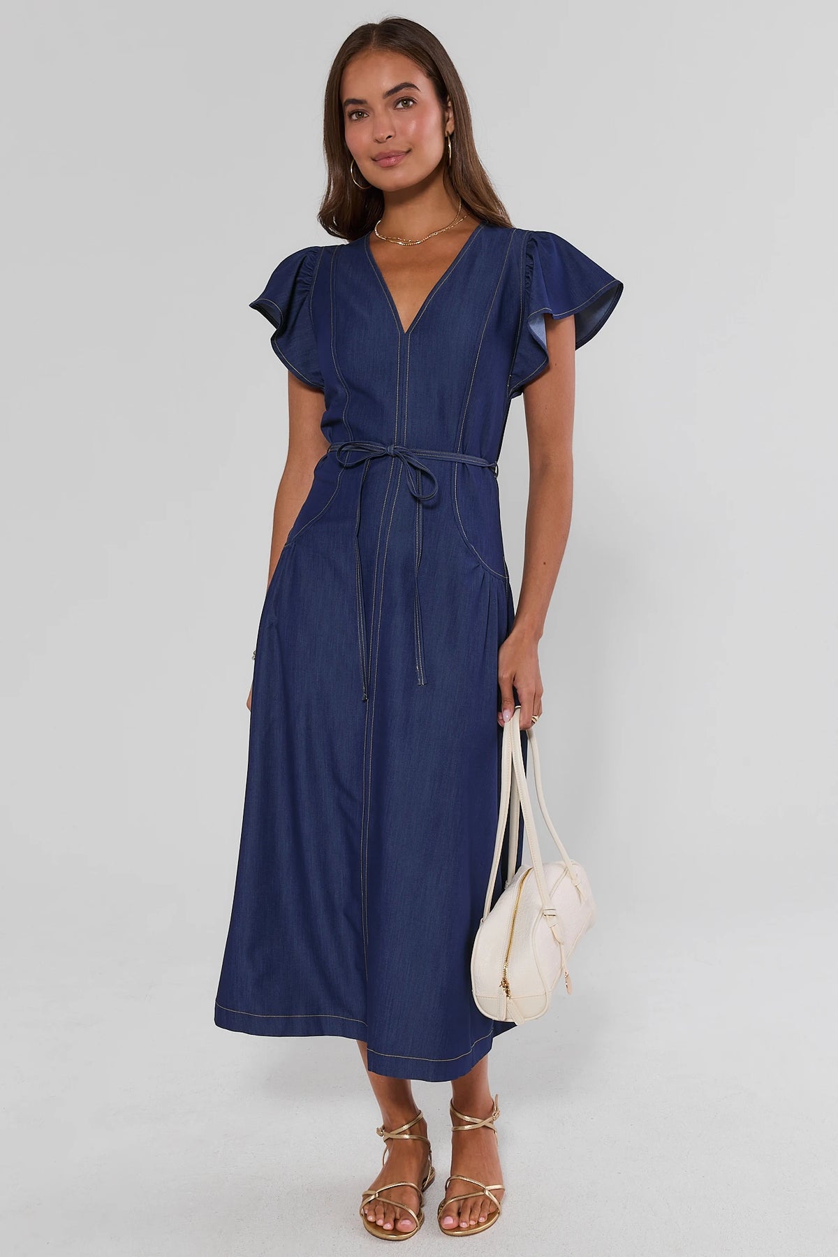 Women's dark blue denim flutter sleeve midi dress styled with gold sandals and cream bag - On Model | Avara