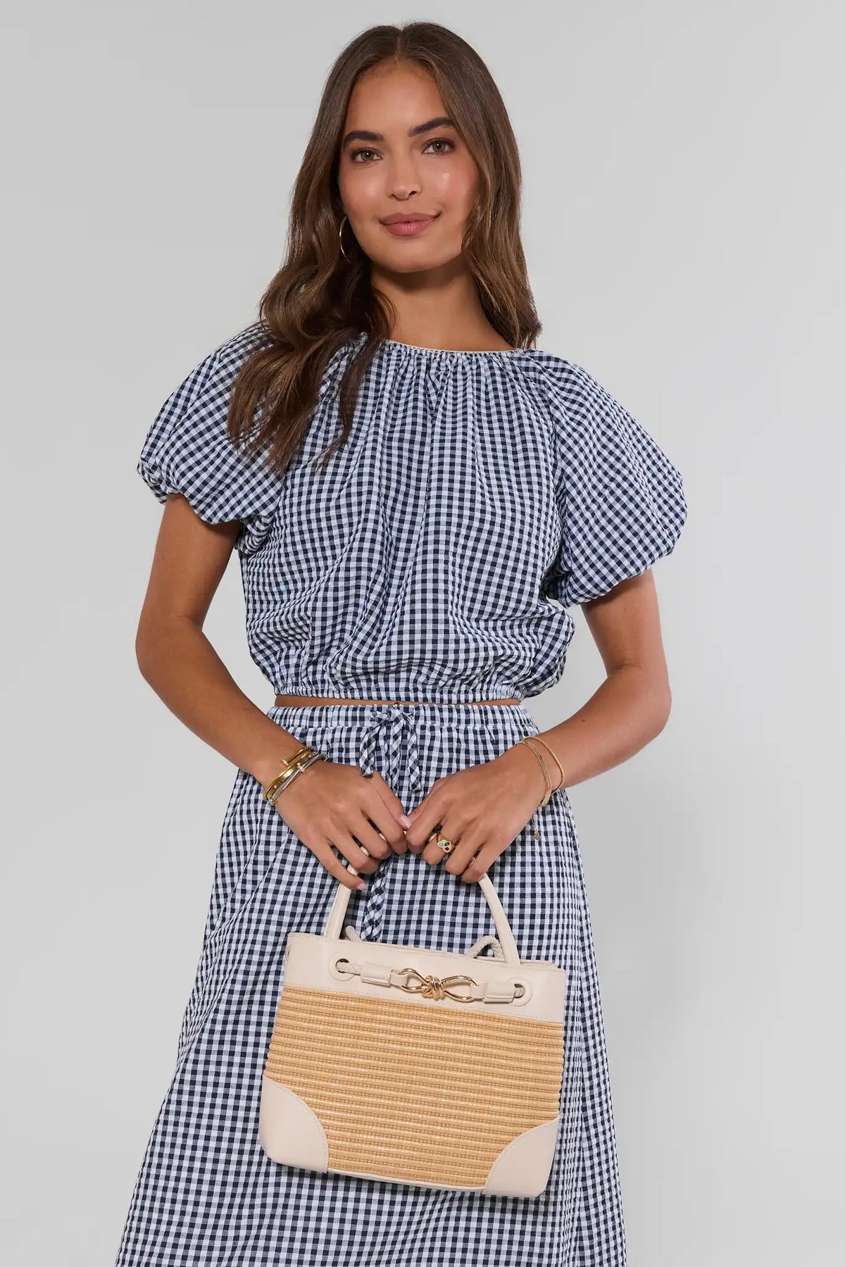 Woman in blue gingham dress holding tan raffia leather trim bag - Front On Model | Avara
