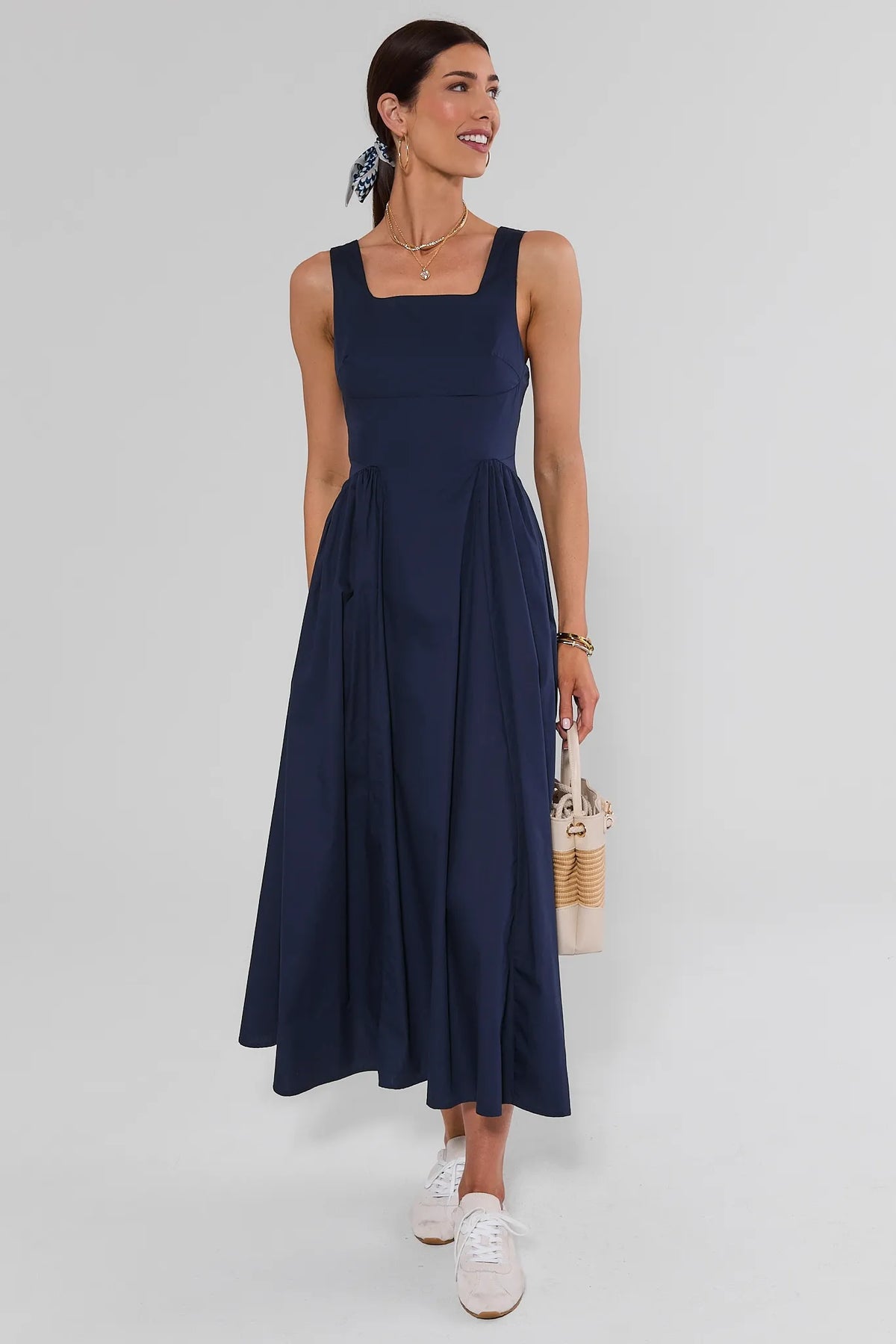 Navy gathered maxi dress styled with white sneakers and woven bag, full-length front view | Avara