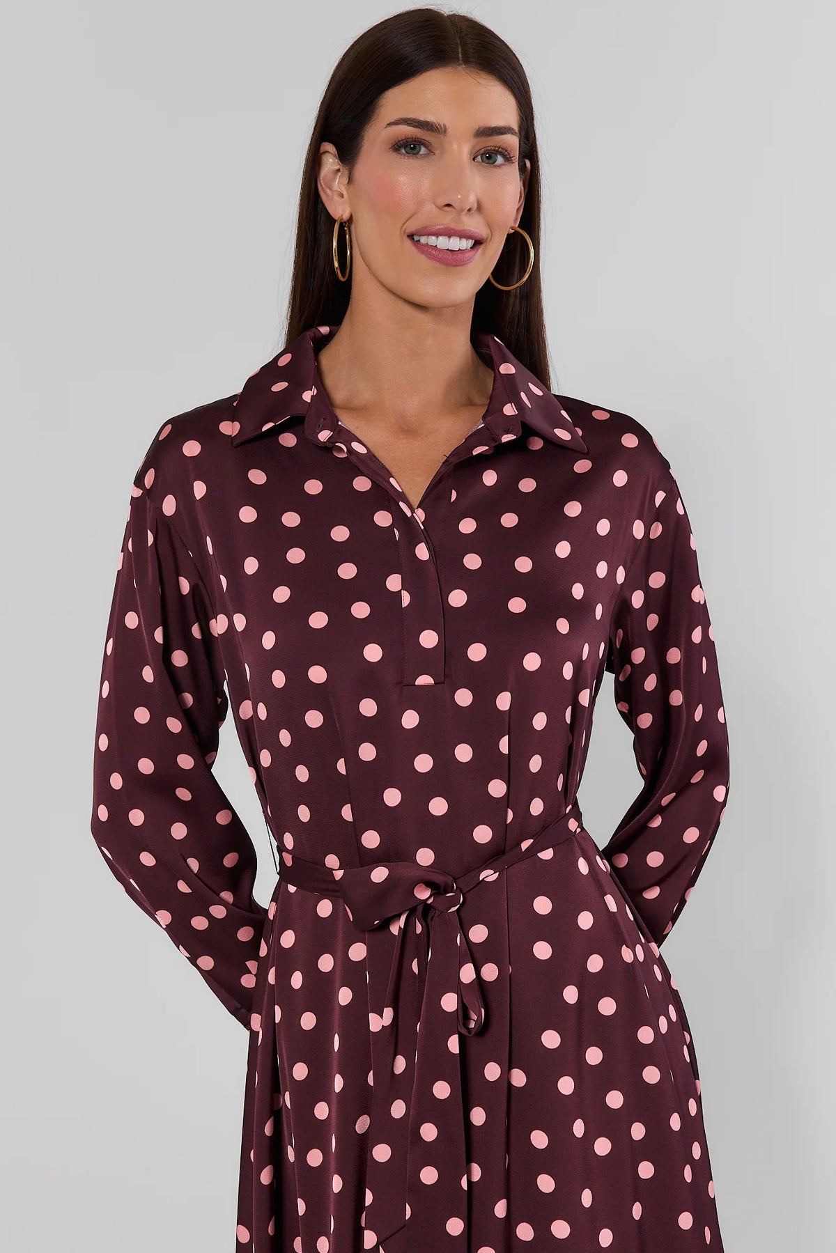 Close-up front detail of brown polka dot midi dress with spread collar, long sleeves, and tie waist on model | Avara