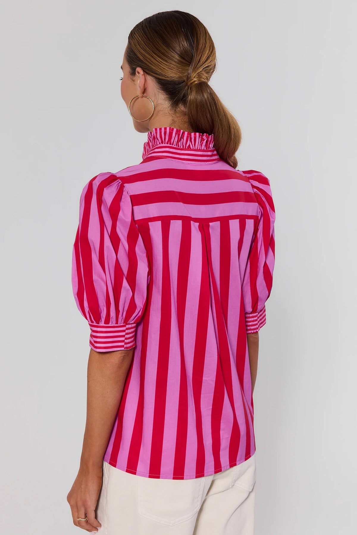 Back view of pink and red striped puff-sleeve top with ruffled high neck, paired with white pants | Avara