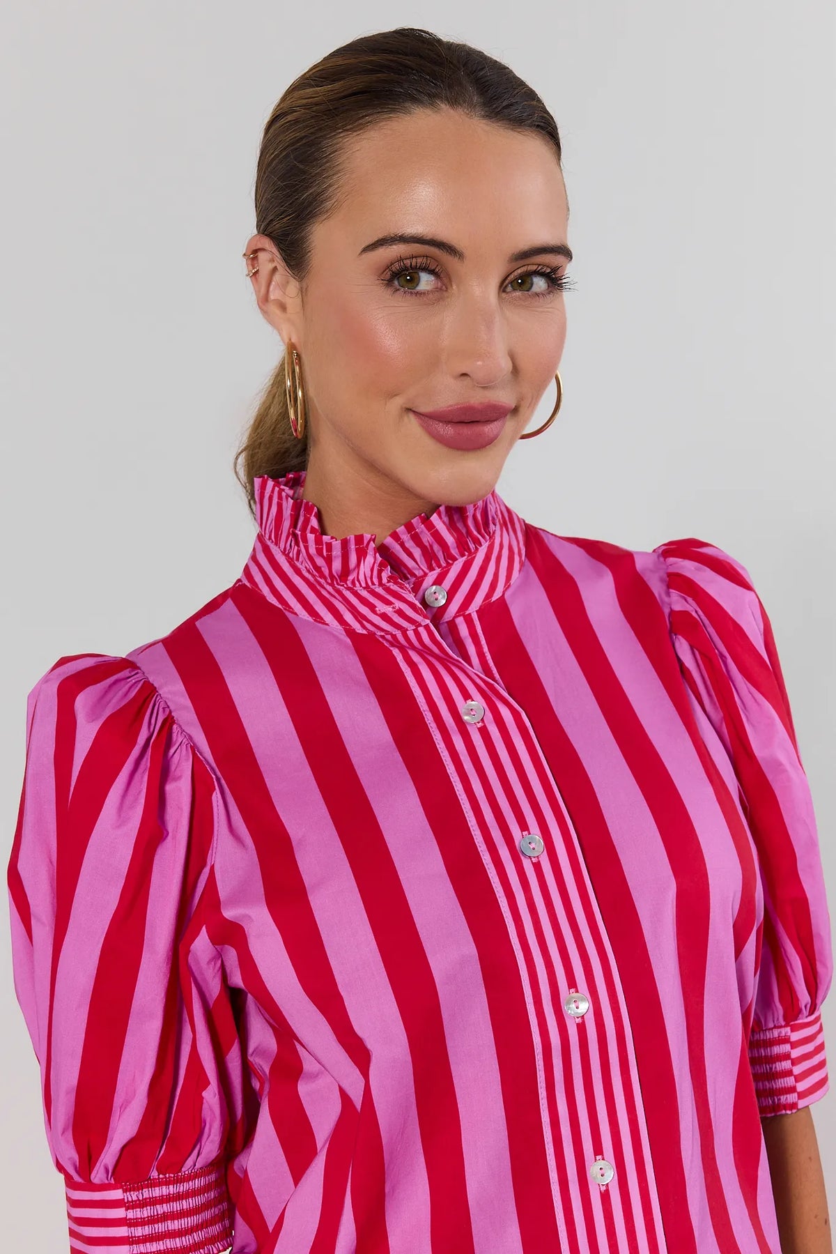 Close-up of pink and red striped button-up top with ruffled collar and smocked cuffs, on model | Avara