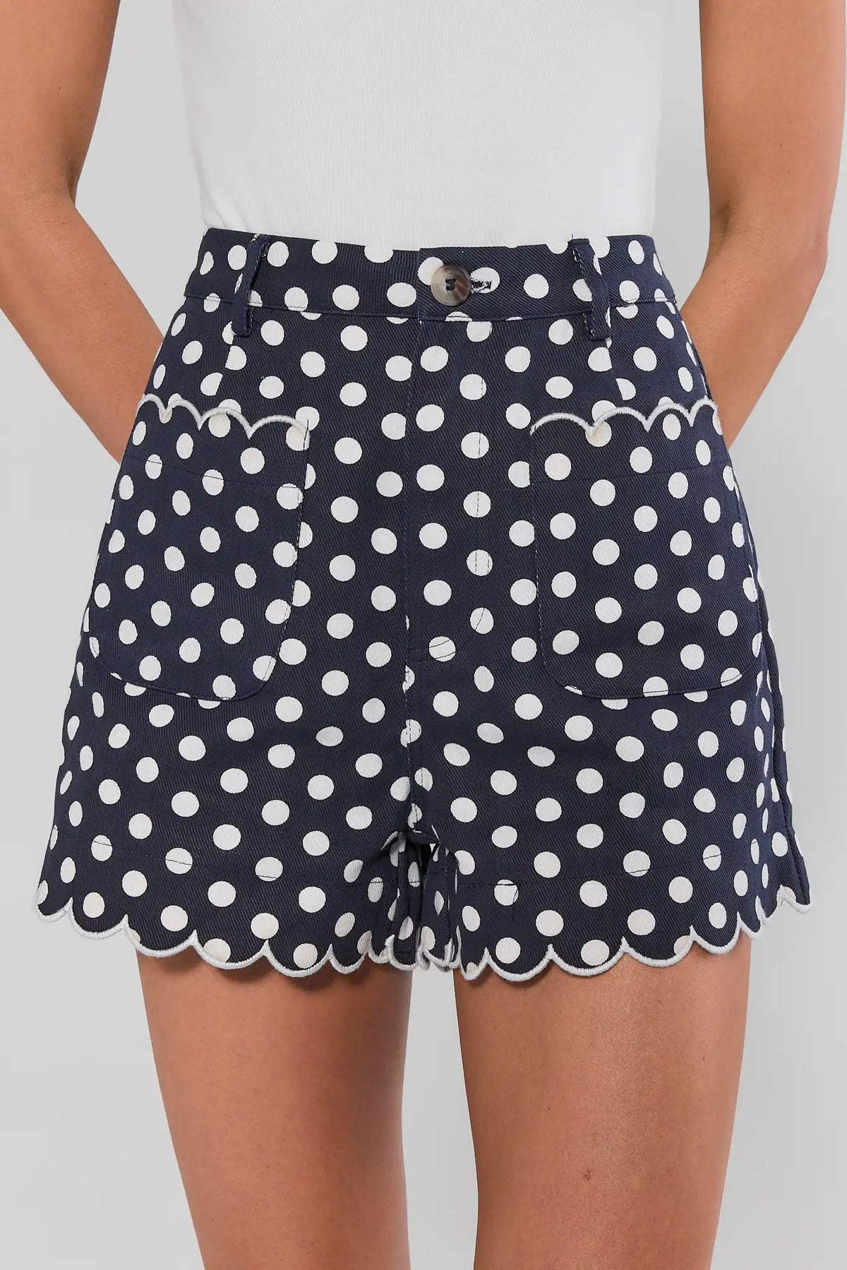 Navy polka dot scalloped shorts back view with white-trimmed hem detail, on model with white top | Avara