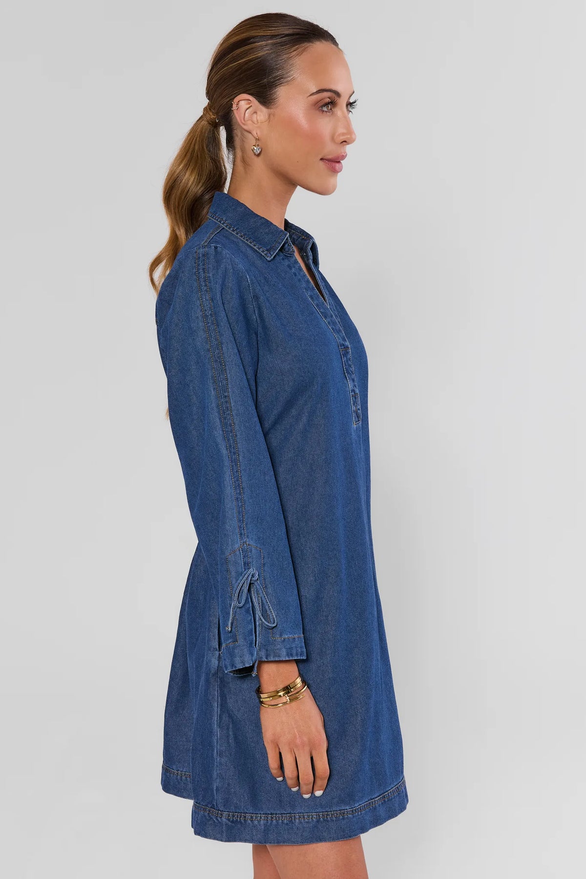 Woman wearing Shay Denim Mini Dress showing side profile, long sleeves with tie detail - Side View | Avara