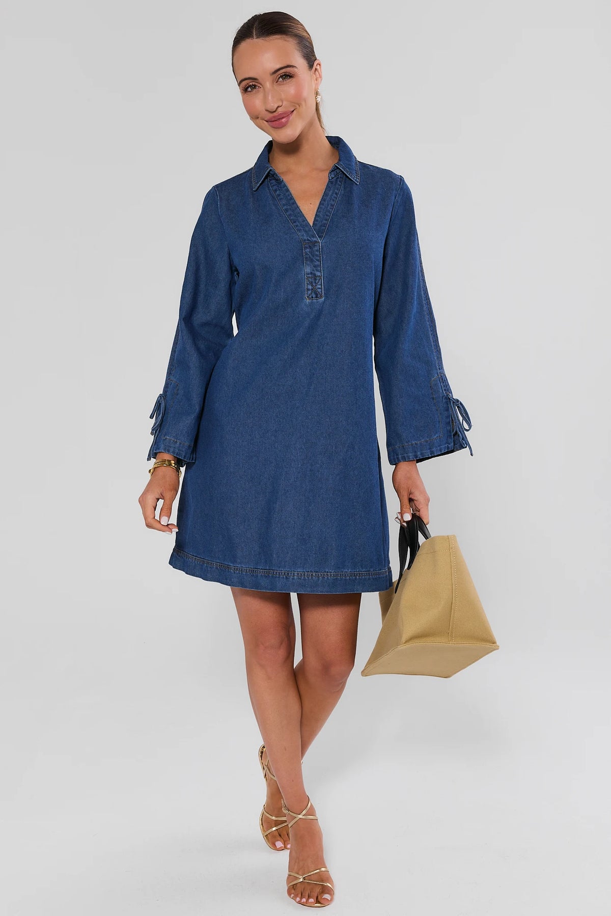 Woman walking in Shay Denim Mini Dress styled with gold sandals and tan tote bag - Full Length View | Avara