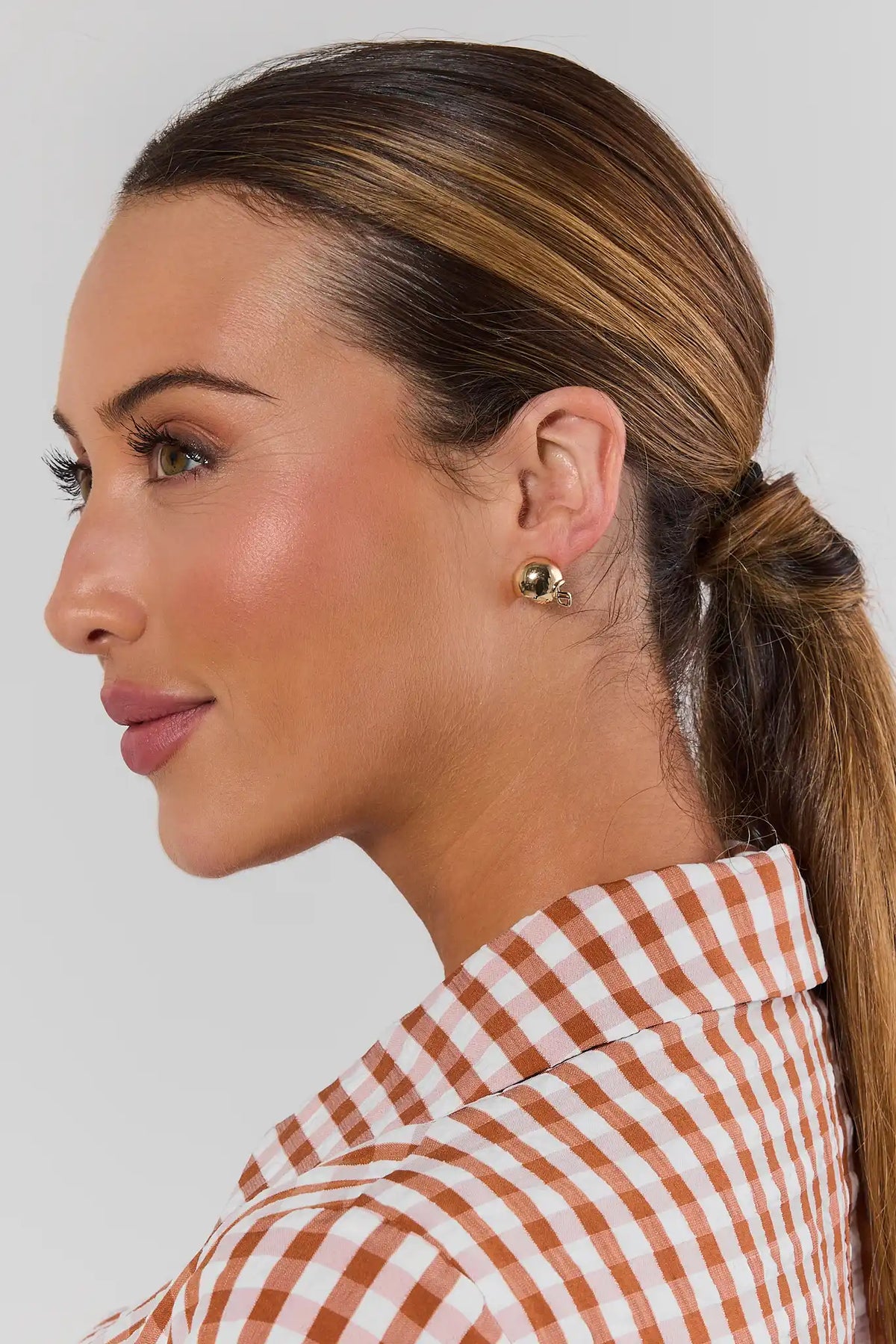 Side profile of woman in gingham shirt wearing gold football helmet earring, game day style | Avara
