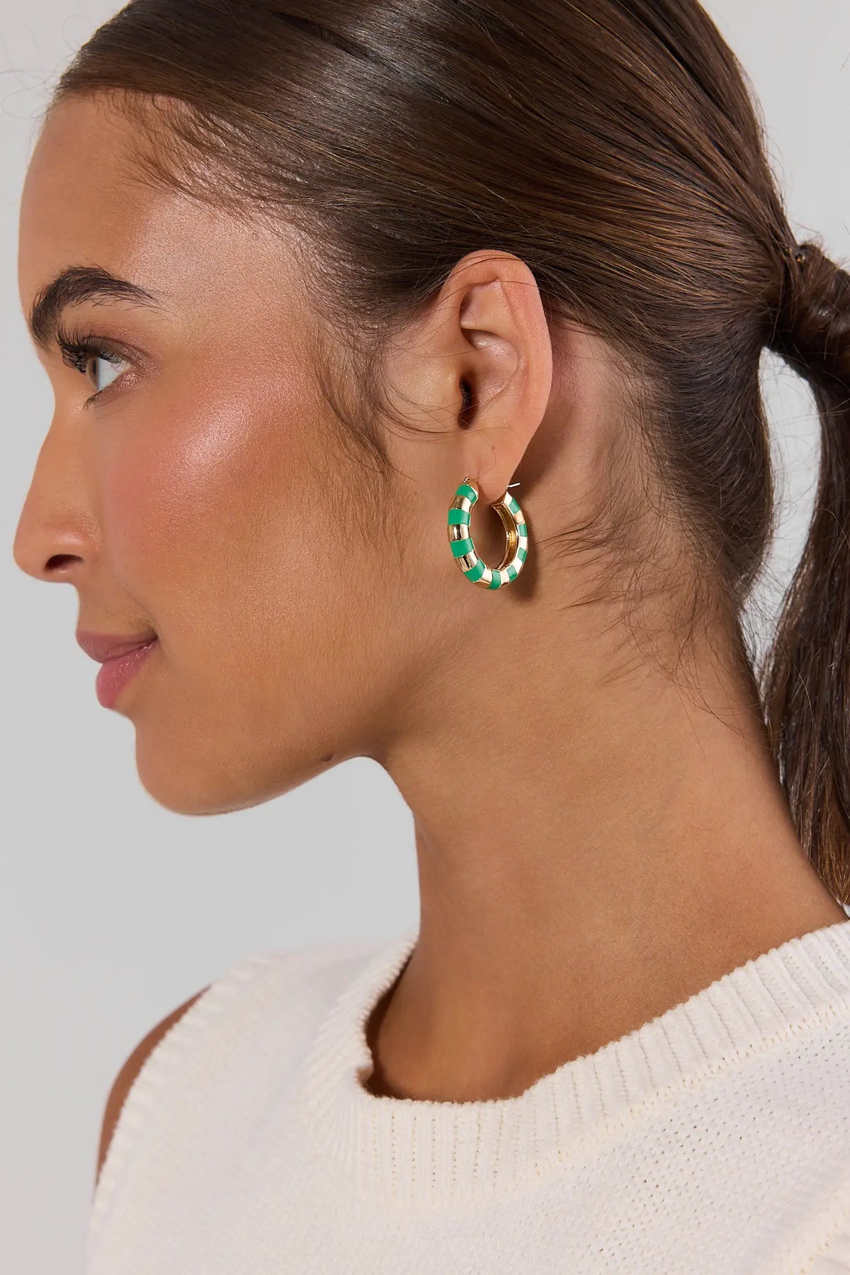 Model wearing green striped gold hoop earrings with white knit top, side profile close-up | Avara