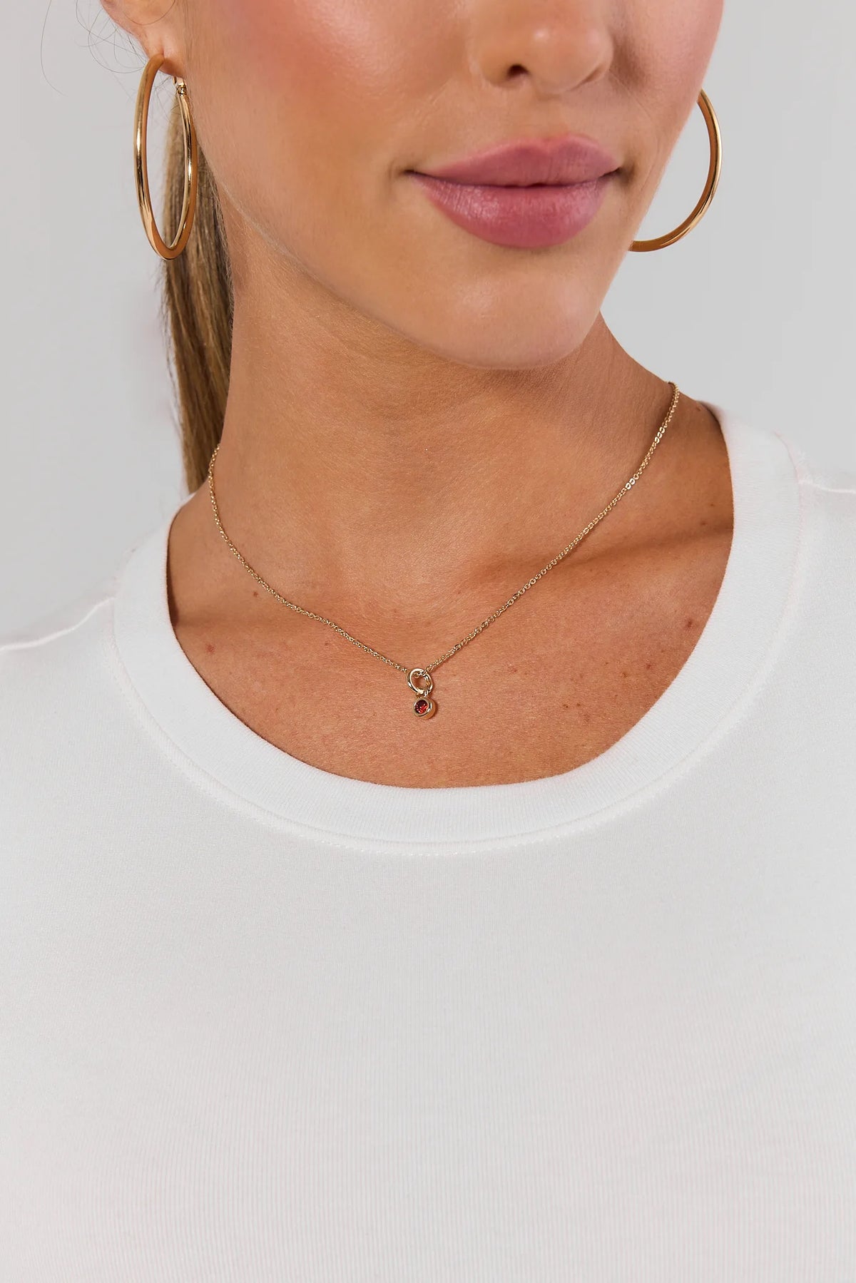 Red Rhinestone Charm on gold chain necklace styled with gold hoop earrings and white top - On Model | Avara