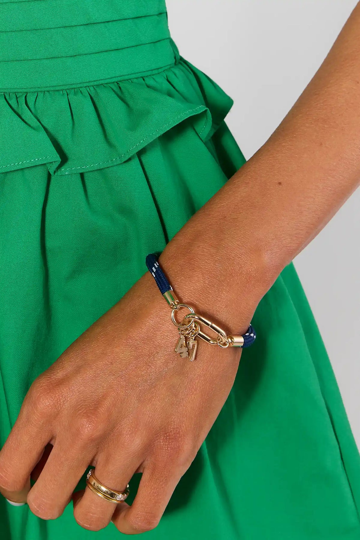 Gold game day number charm on navy rope bracelet on model wrist, styled game day outfit look | Avara