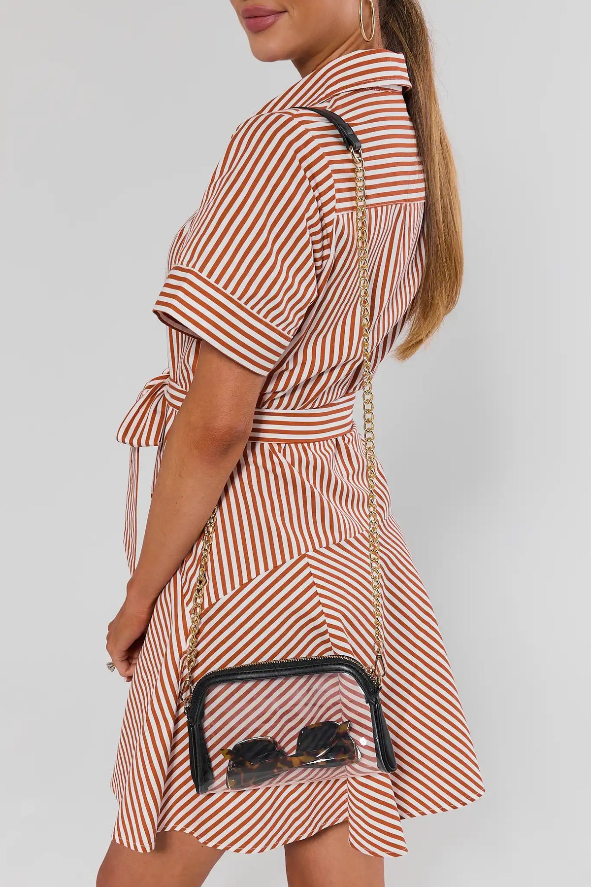 Woman in rust striped dress carrying clear stadium-approved crossbody bag with black trim - On Model | Avara