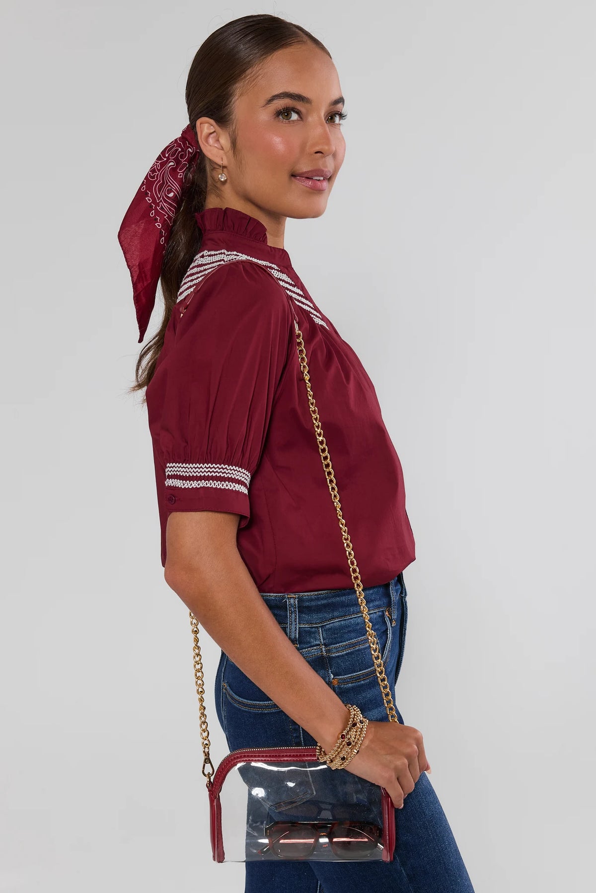 Woman in maroon top and jeans wearing a maroon clear crossbody bag with gold chain - Styled Look | Avara