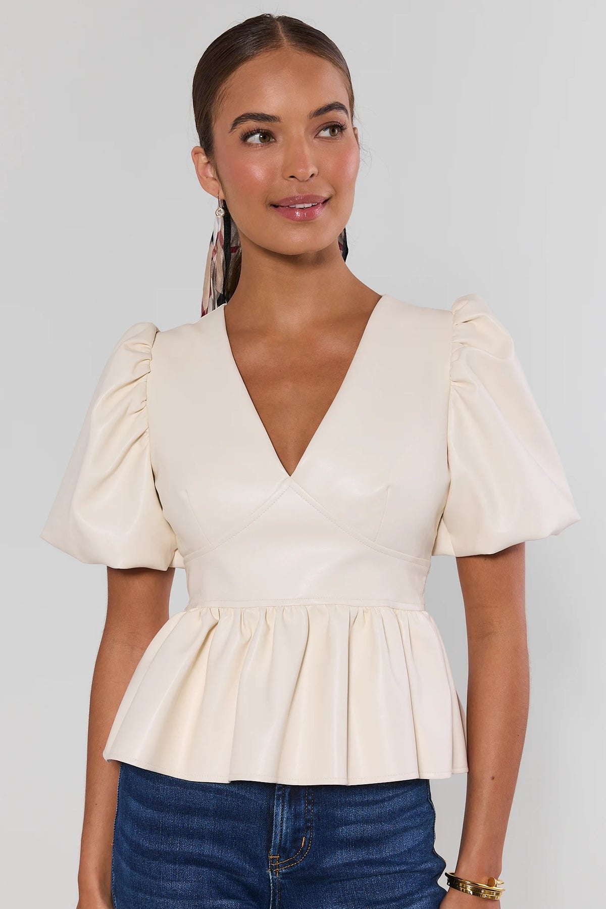 Ivory faux leather peplum top with puff sleeves paired with dark jeans and woven flats - Front View | Avara