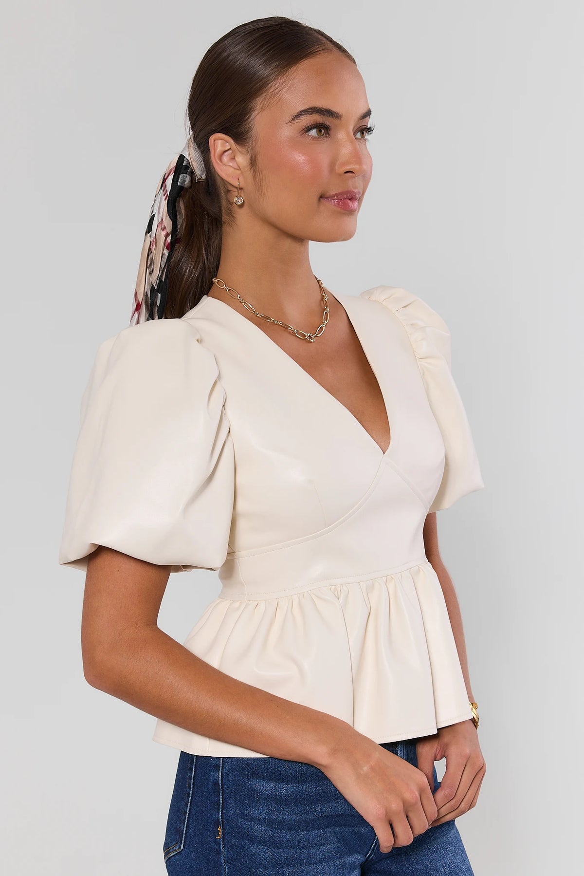 Ivory faux leather peplum top with puff sleeves and plaid hair scarf, paired with dark jeans - 3/4 View | Avara