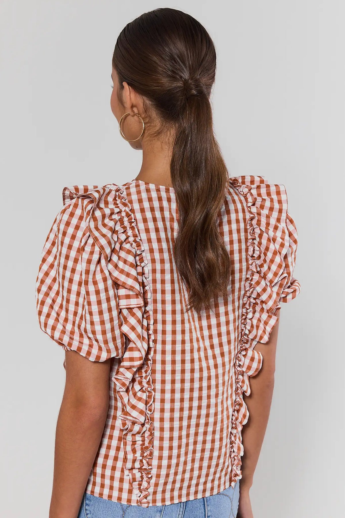 Back view of orange gingham ruffle top showing ruffle trim detailing and puff sleeves, paired with jeans | Avara
