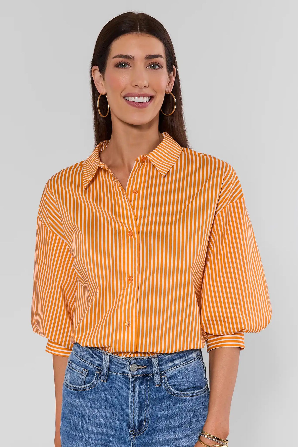 Orange striped button-up top with voluminous puff sleeves, paired with blue jeans - Front Smiling View | Avara