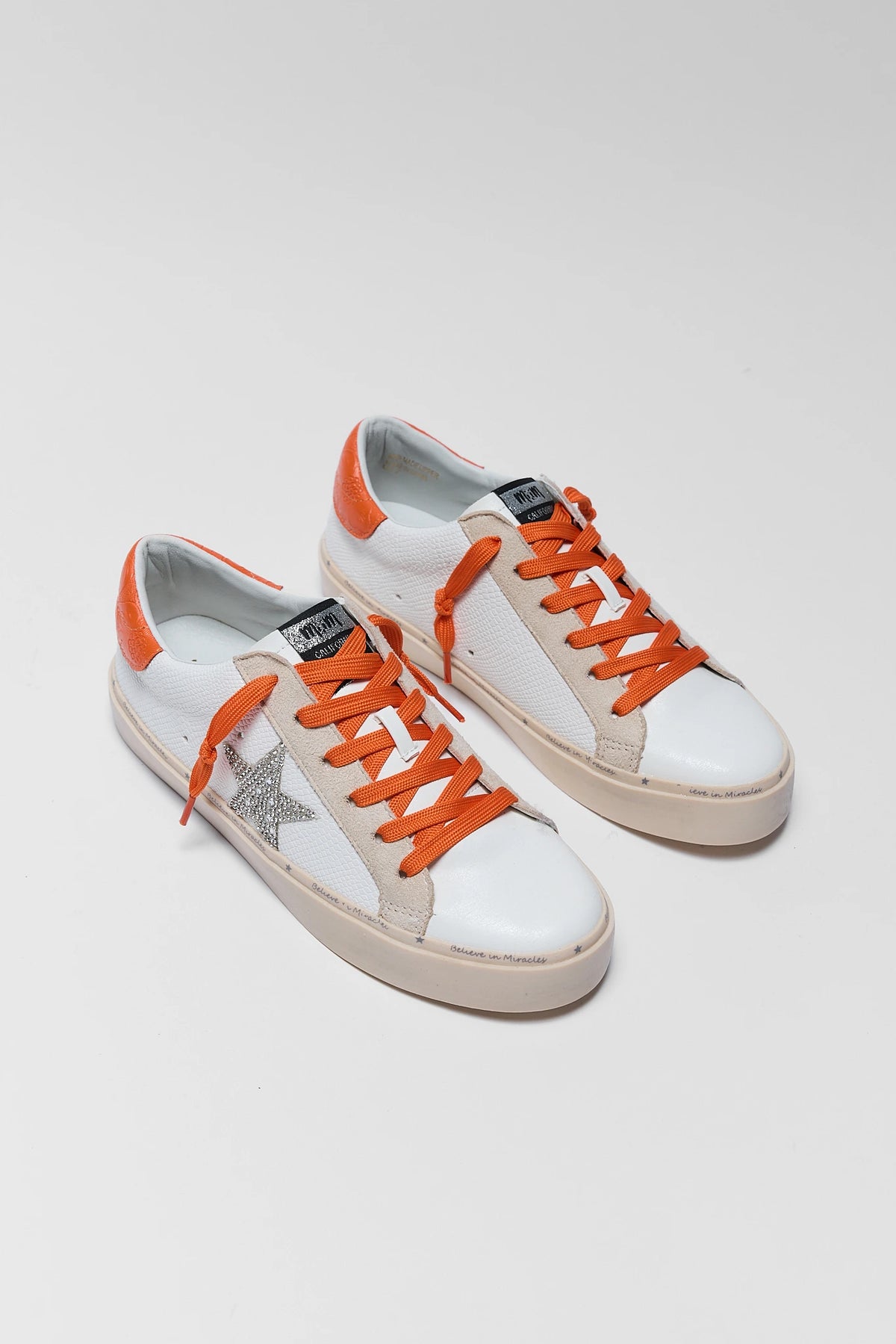 Pair of white and silver star sneakers with orange laces and orange heel tabs - Front Angle | Avara
