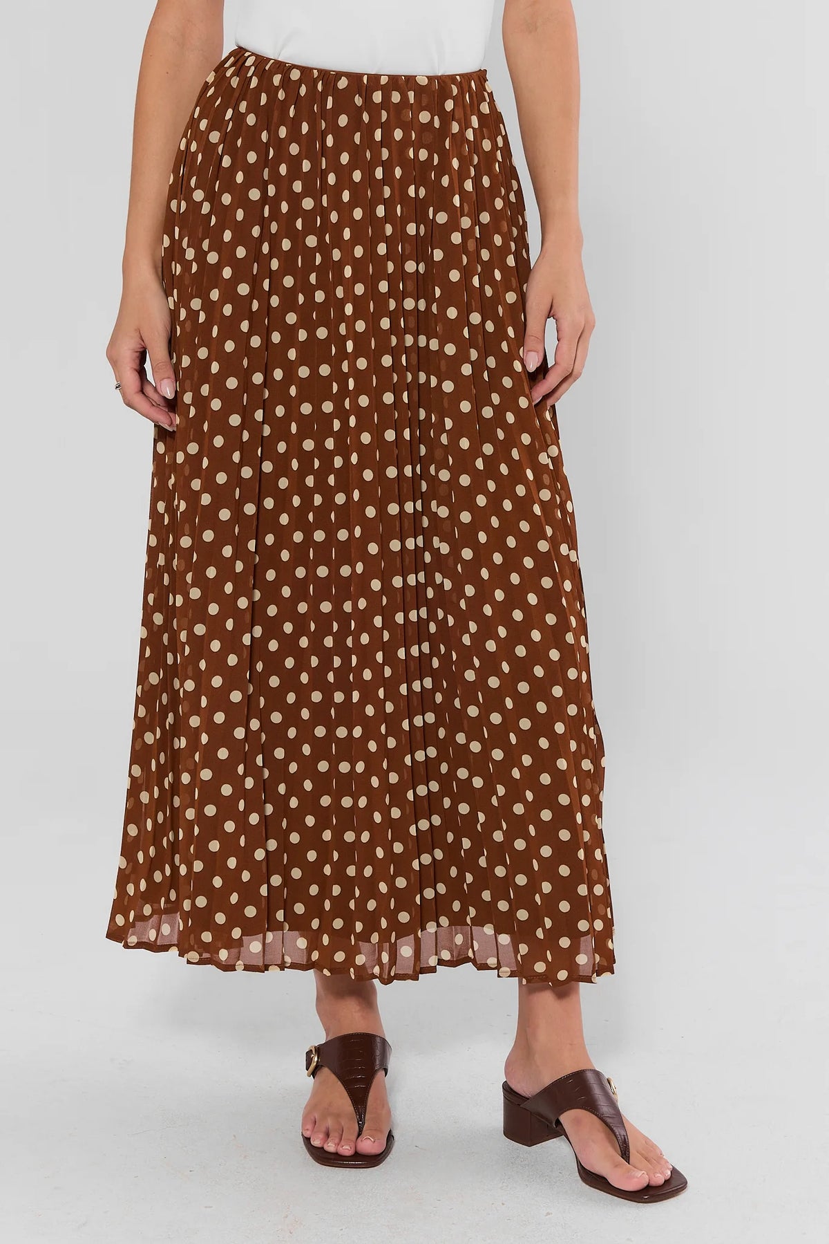 Brown pleated maxi skirt with beige polka dot print, elastic waist, worn with brown sandals - Front Close-Up | Avara