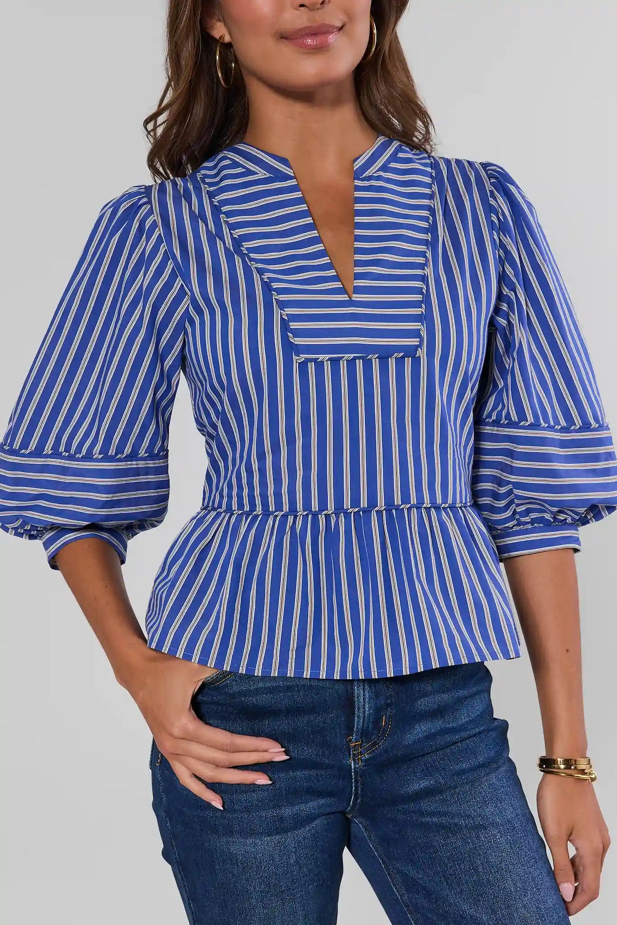 Blue striped split neck peplum top with balloon sleeves, three-quarter front view, styled with jeans | Avara