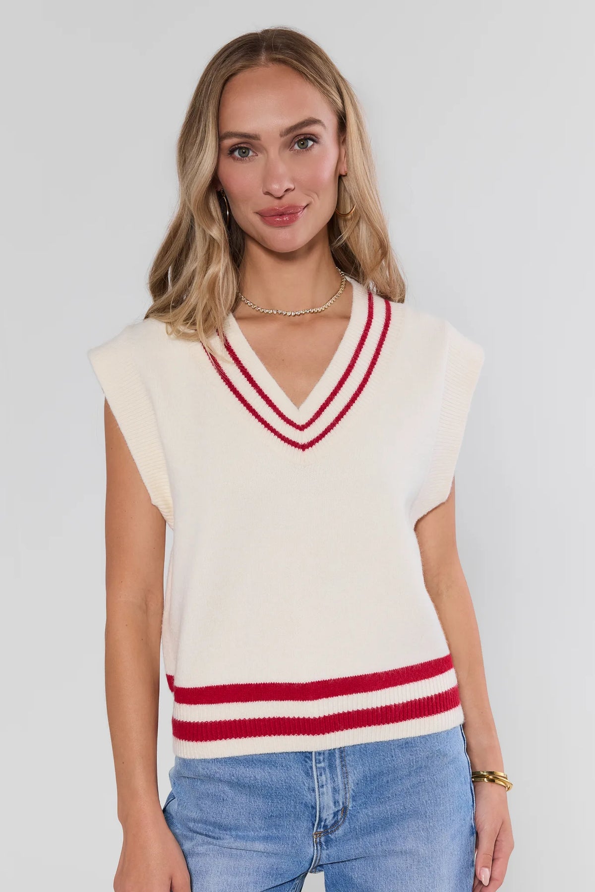 White knit sweater vest with red contrast stripe V-neck and hem trim, styled with blue jeans - Front View | Avara