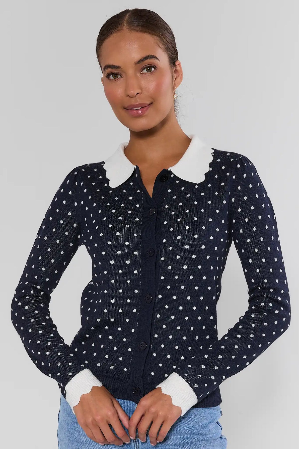 Navy polka dot cardigan sweater with white Peter Pan collar and ribbed cuffs, paired with light blue jeans - Front View | Avara