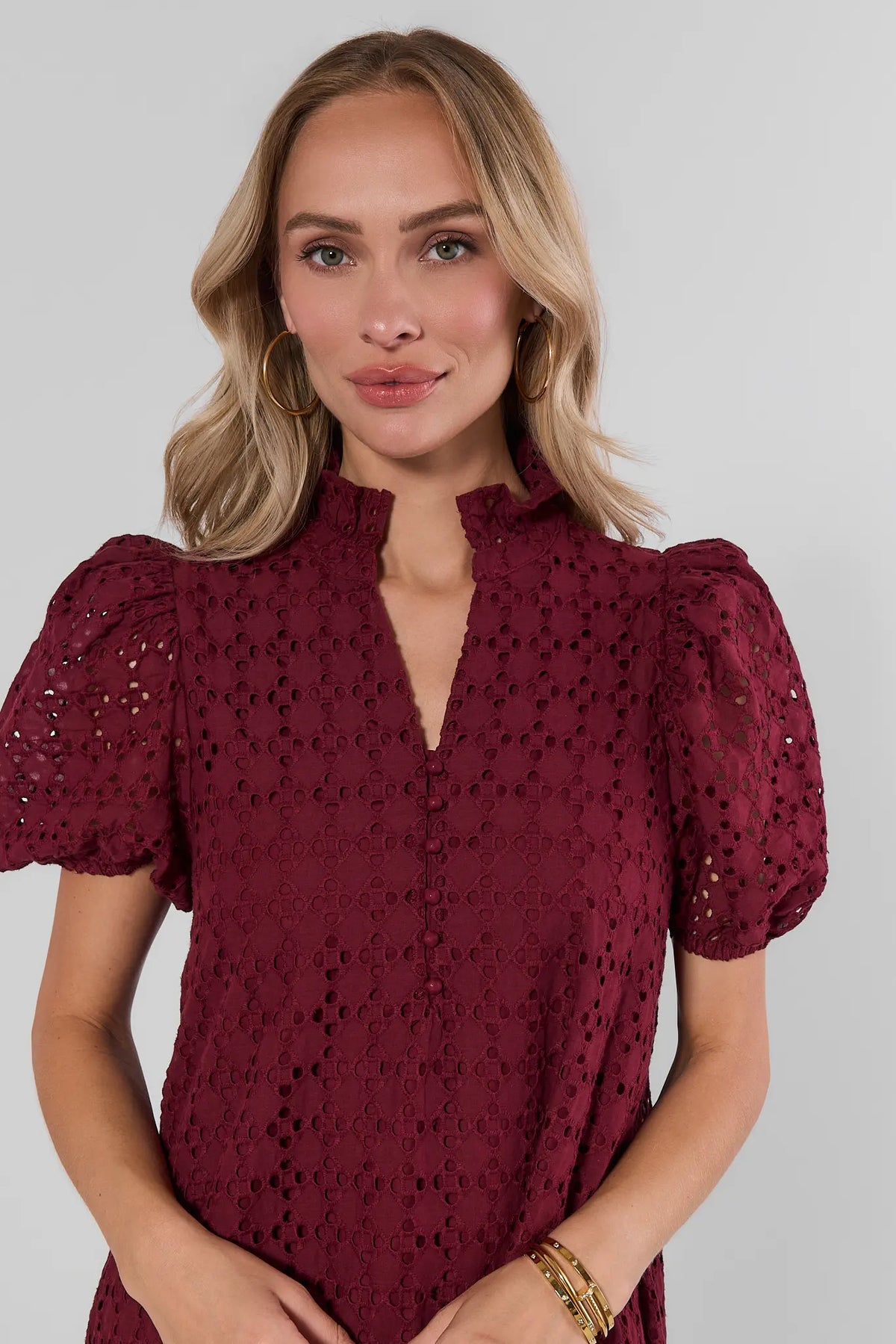 Burgundy eyelet dress close-up detail, puff sleeves and V-neckline with button placket, gold hoop earrings | Avara