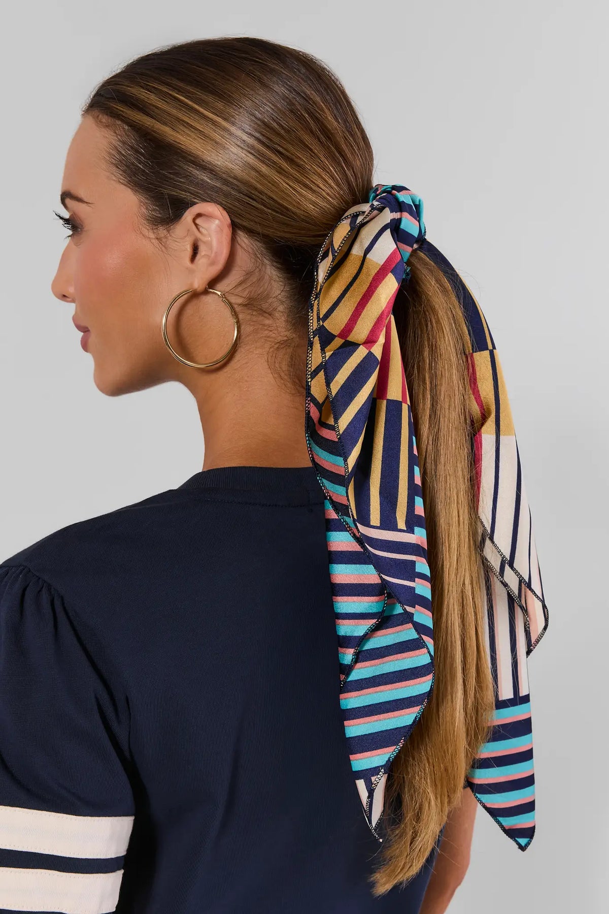 Mixed Stripe Scarf tied in hair ponytail, multicolor navy teal gold print, styled with gold hoops - Back View | Avara