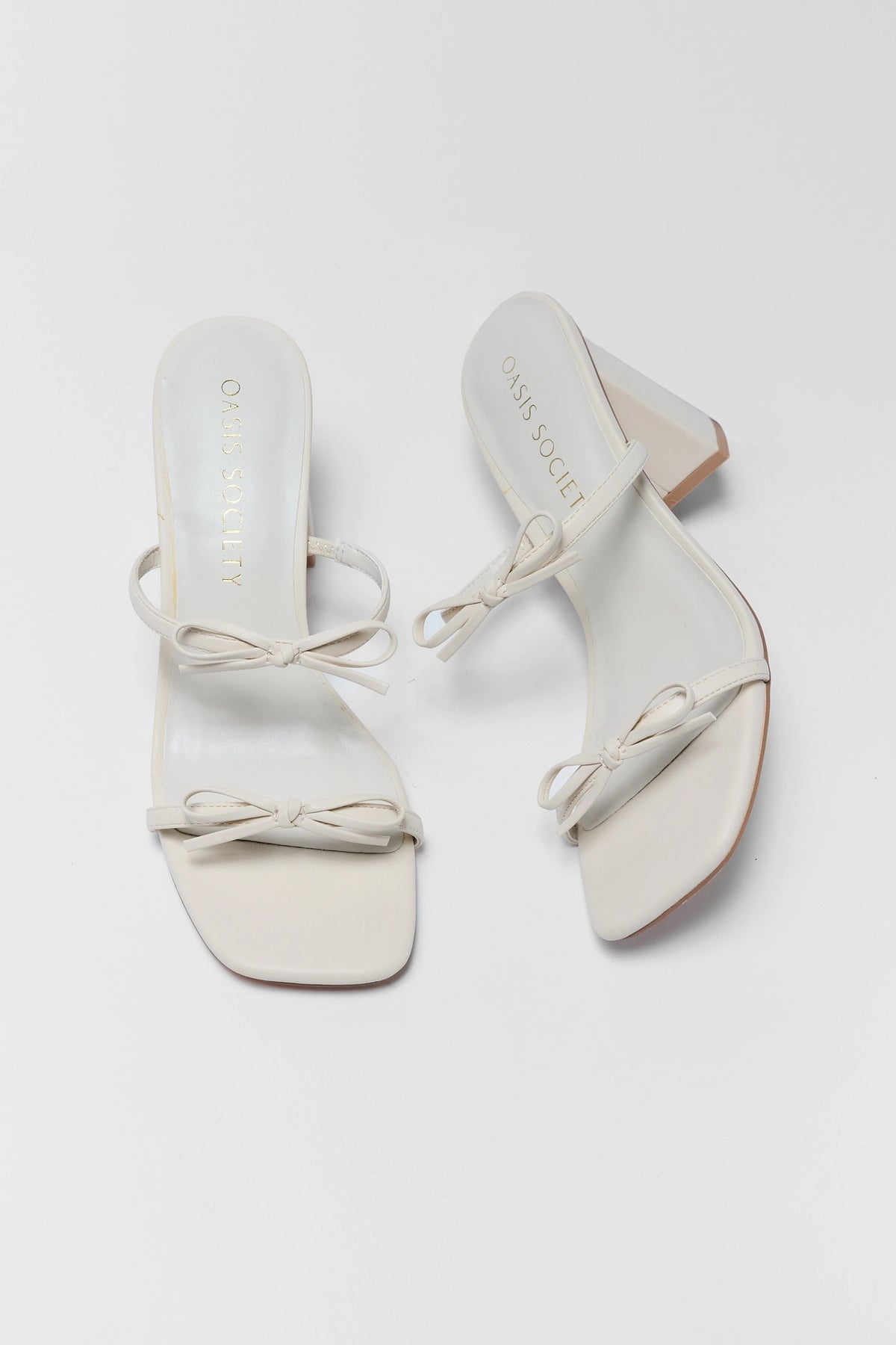 White double-strap bow heels pair with block heel, top-down flat lay view | Avara