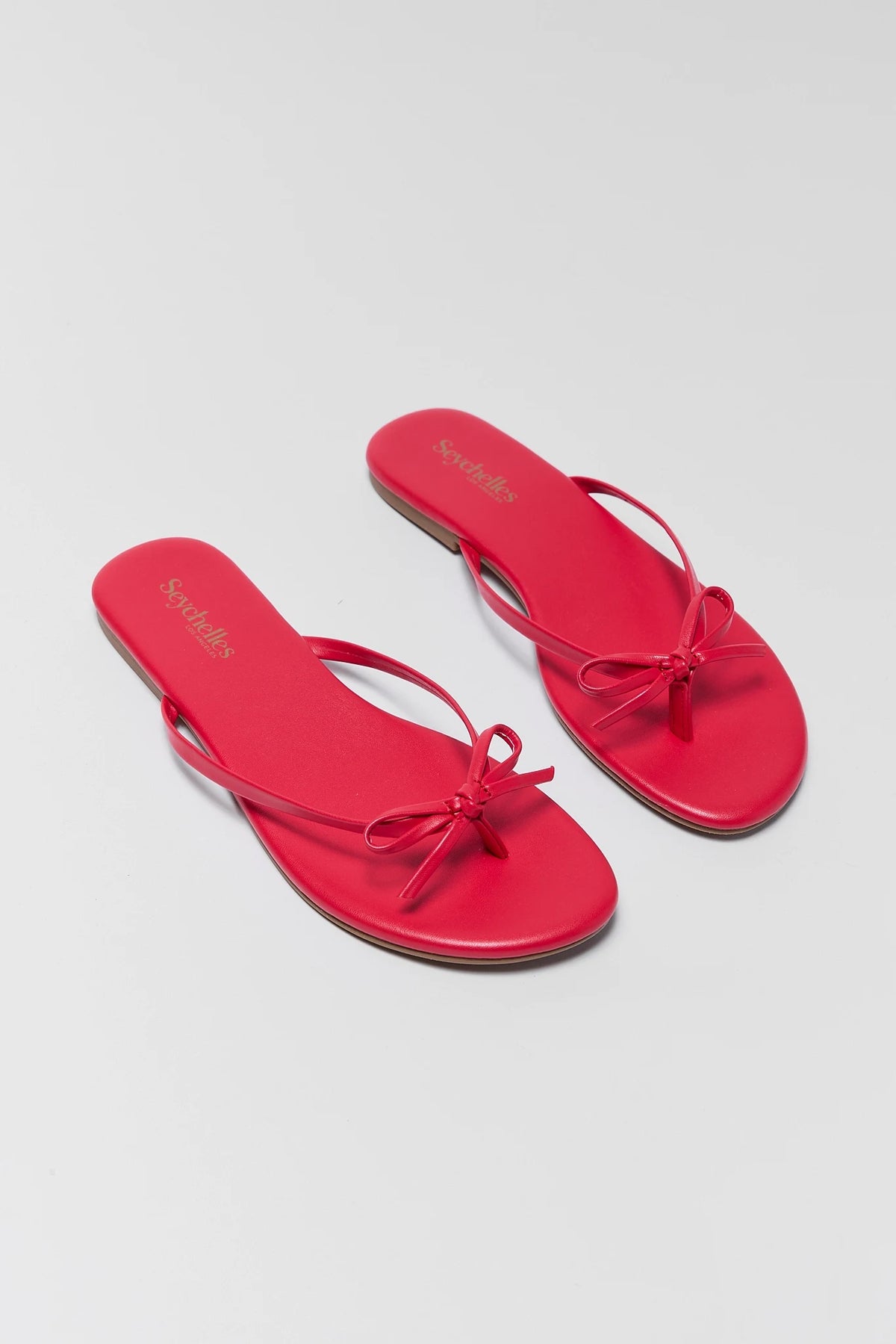 Two red bow sandals with a bow on a light gray background - Overhead Flat Lay | Avara