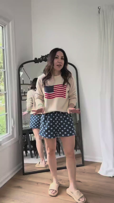 woman wearing cream american flag sweater with mirror in background