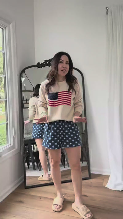 woman wearing cream american flag sweater with mirror in background