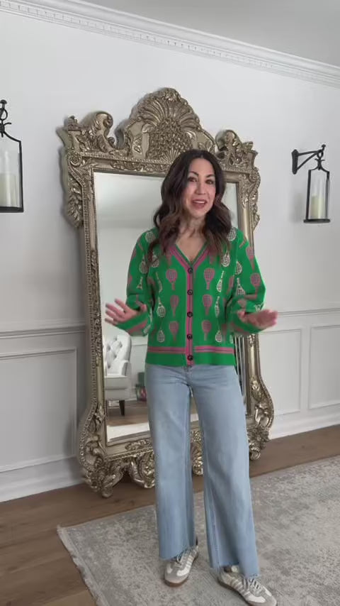woman wearing a green cardigan with tennis rackets with a mirror in the background