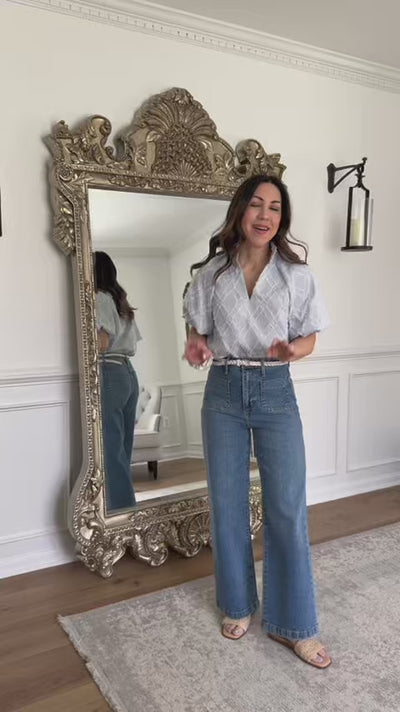 woman wearing a blue blouse with jeans with mirror in background